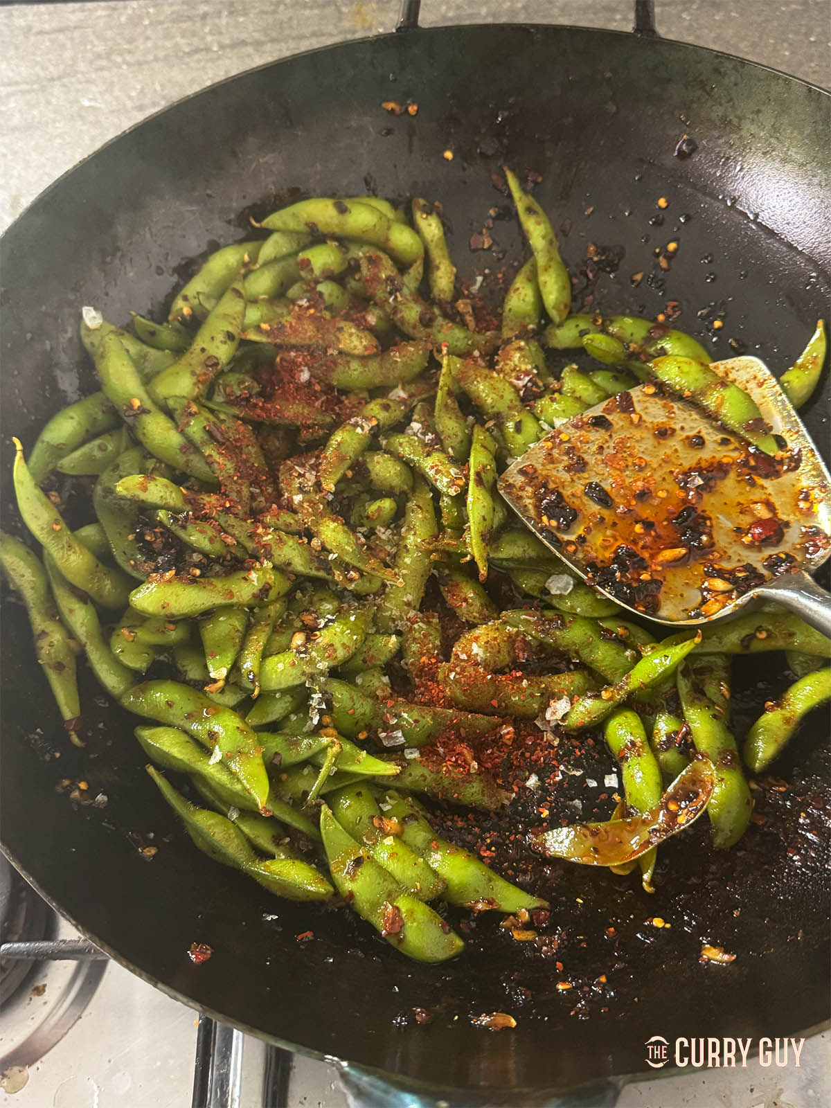 Stirring the edamame into the sauce in the wok.