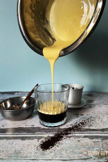 The creamy egg yolk mixture being poured over freshly brewed coffee.