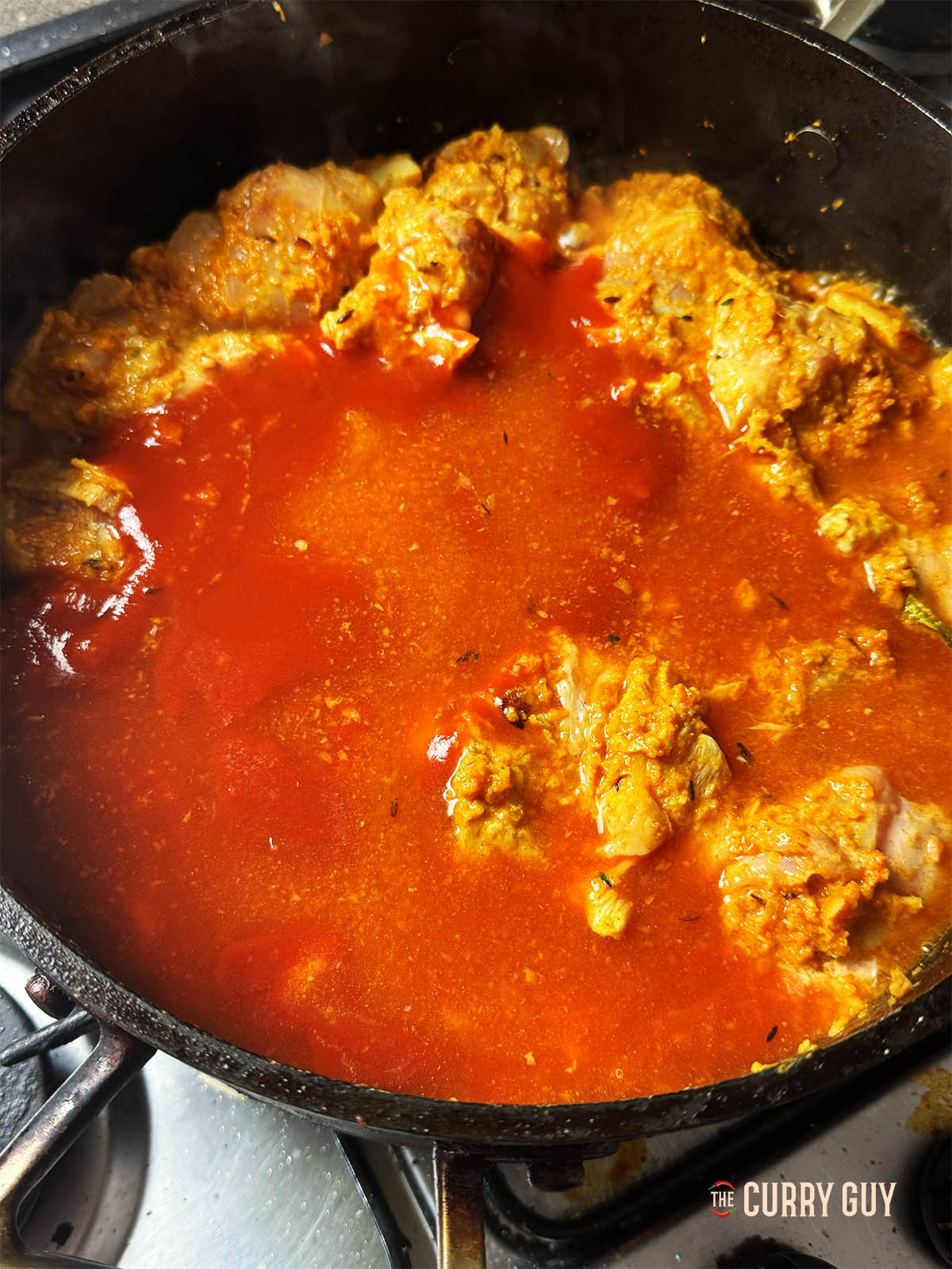 Adding the passata and chicken stock to the pan to bring to a simmer and cook the chicken.