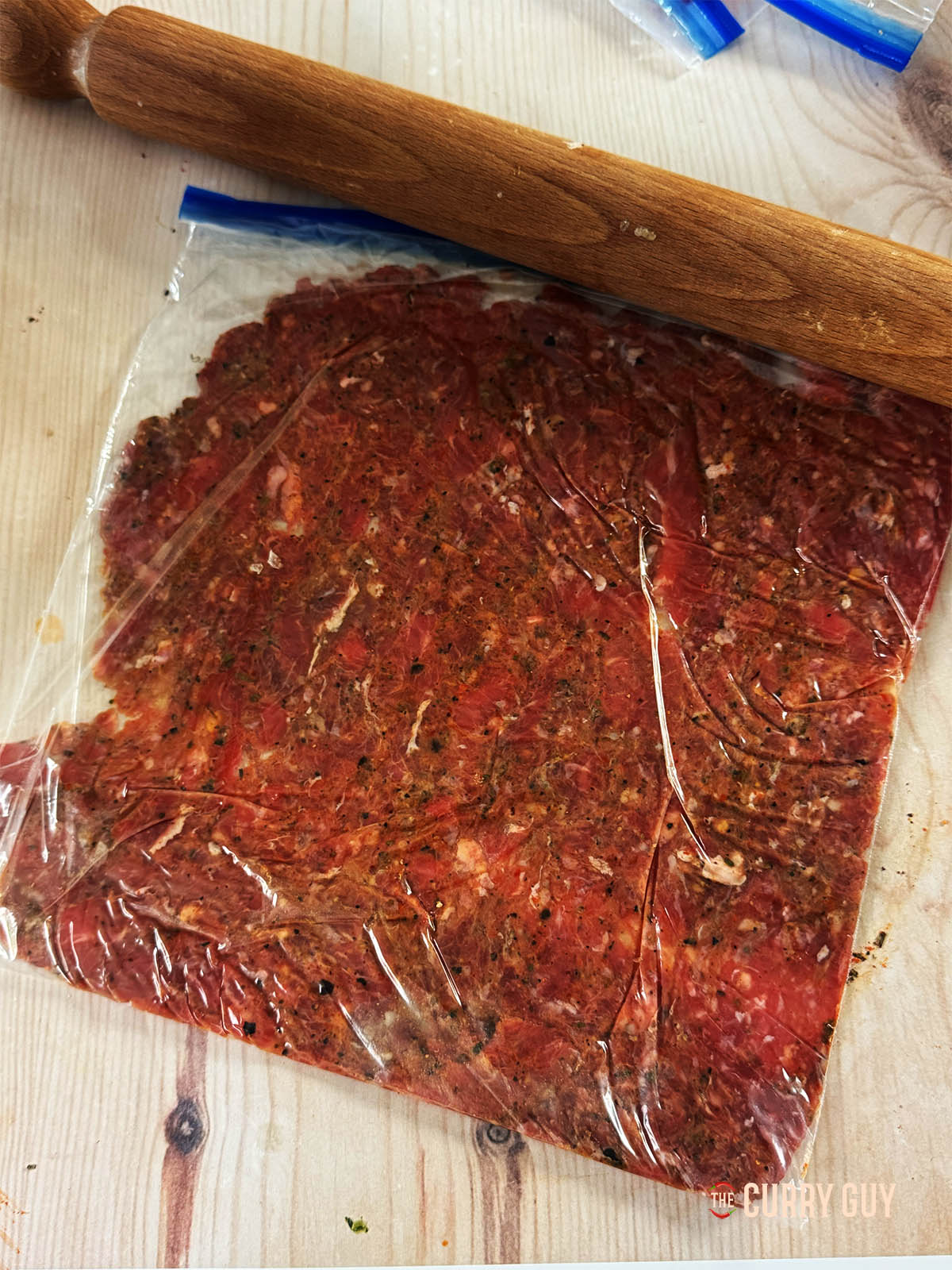 Flattening some of the meat in a freezer bag using a rolling pin.