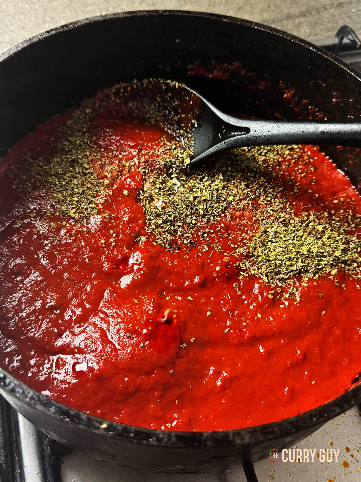 Adding dried herbs to the simmering sauce.