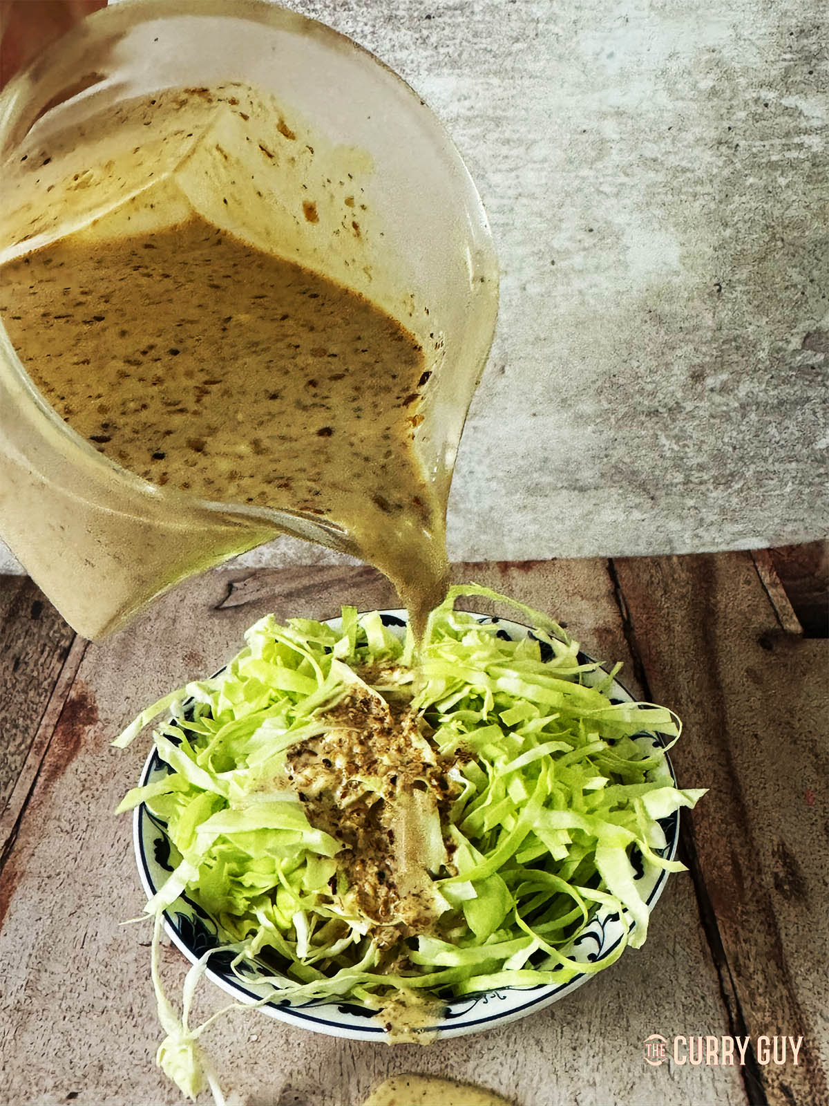 Japanese salad dressing being poured from a jug over cabbage.