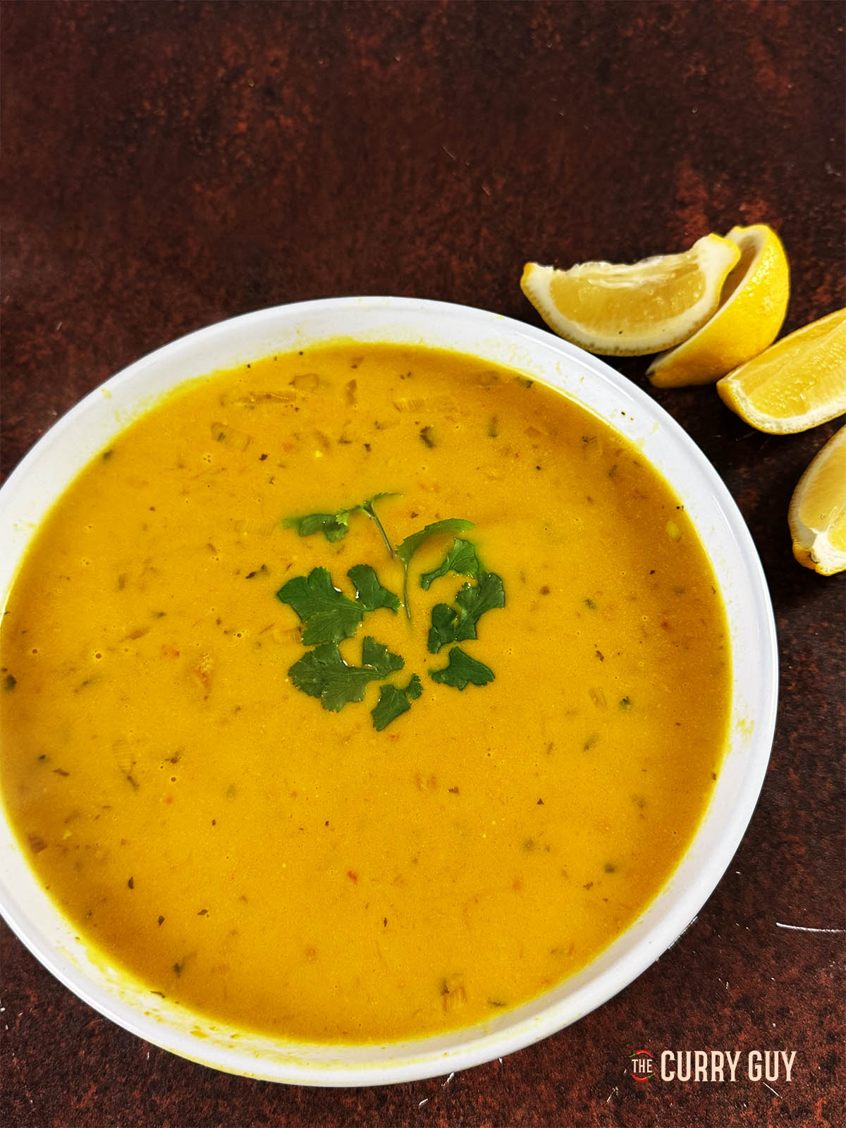 Mulligatawny Soup in a serving bowl with lemons on the side.