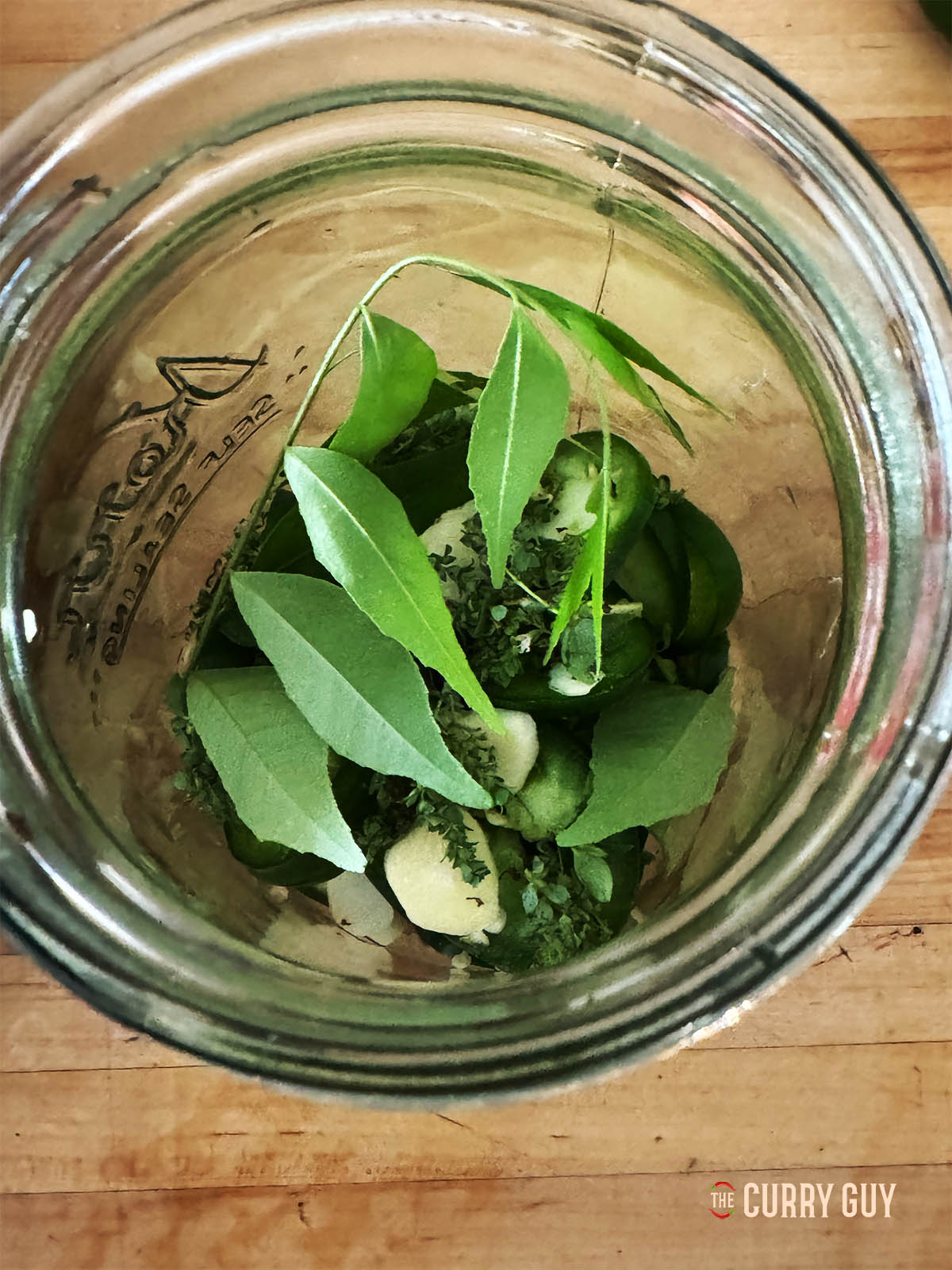 Layering the chillies, garlic and herbs in a preserve jar.