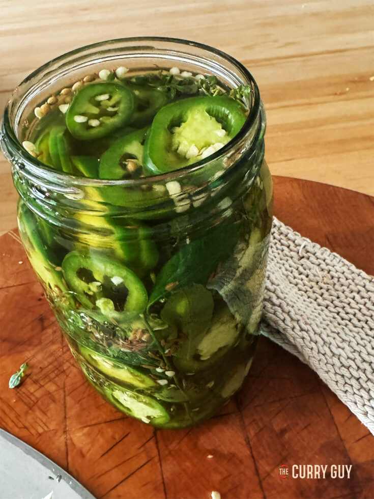 Pickled jalapeños in a preserve jar with the lid off.