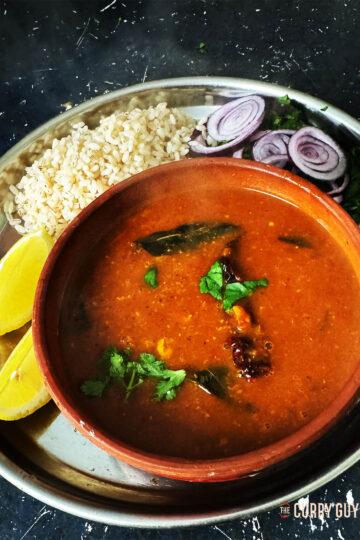 Rasam in a serving bowl with rice, lemon wedges and side salad.