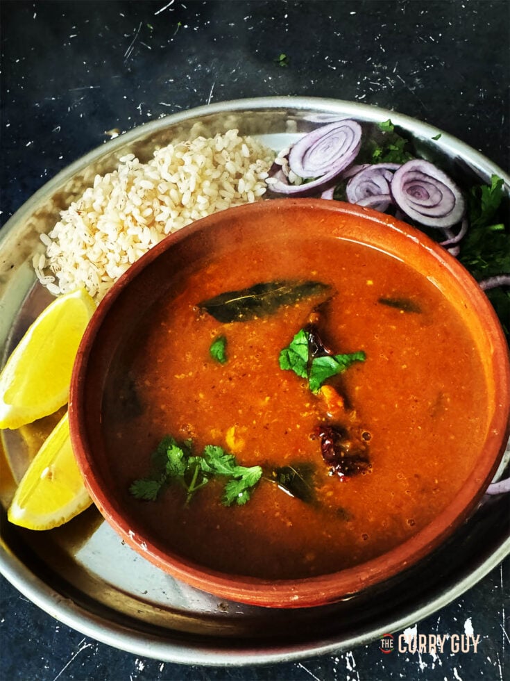 Rasam in a serving bowl with rice, lemon wedges and side salad.