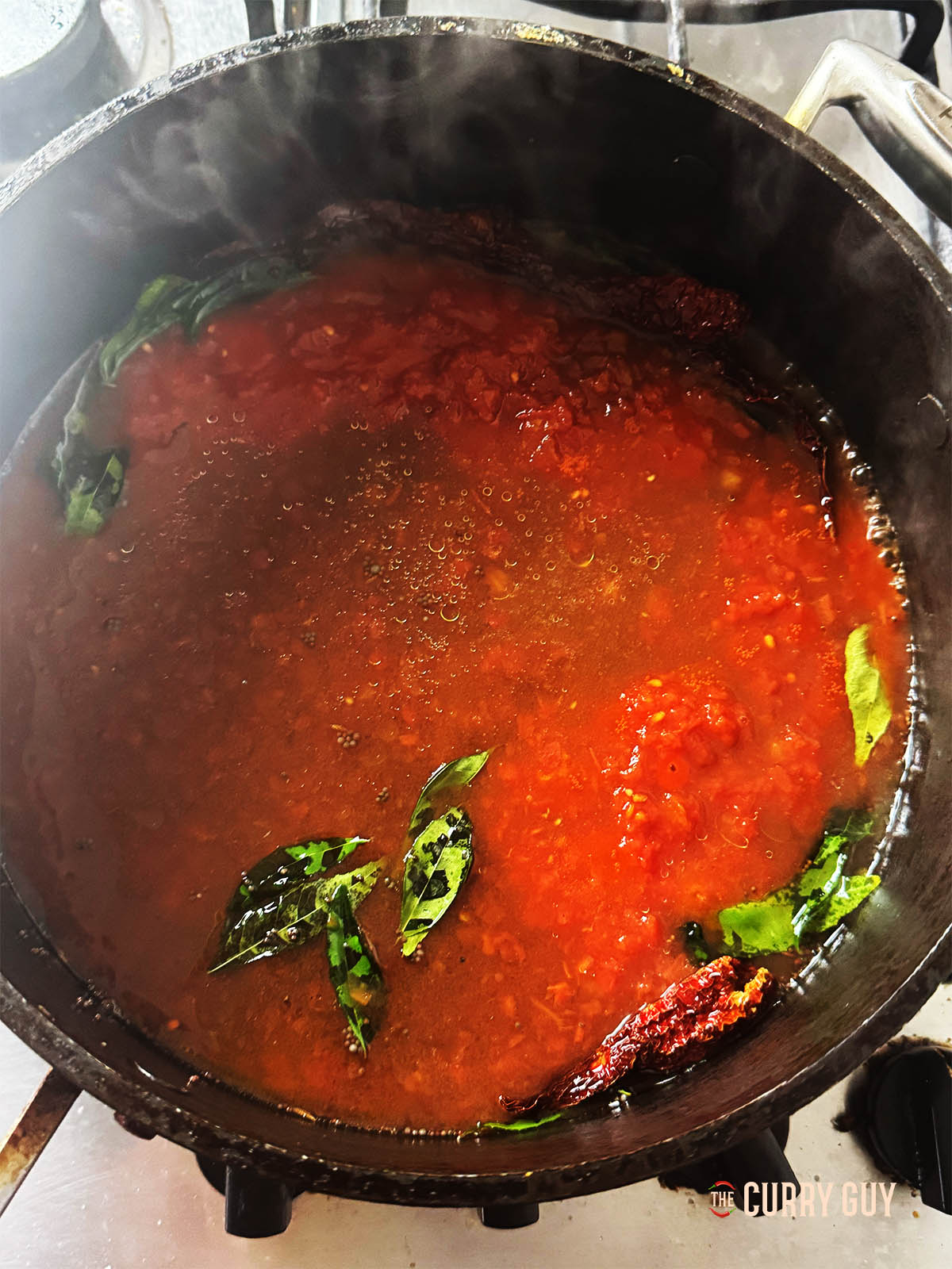 Adding the garlic and spice paste along with the chopped tomatoes and tamarind water.