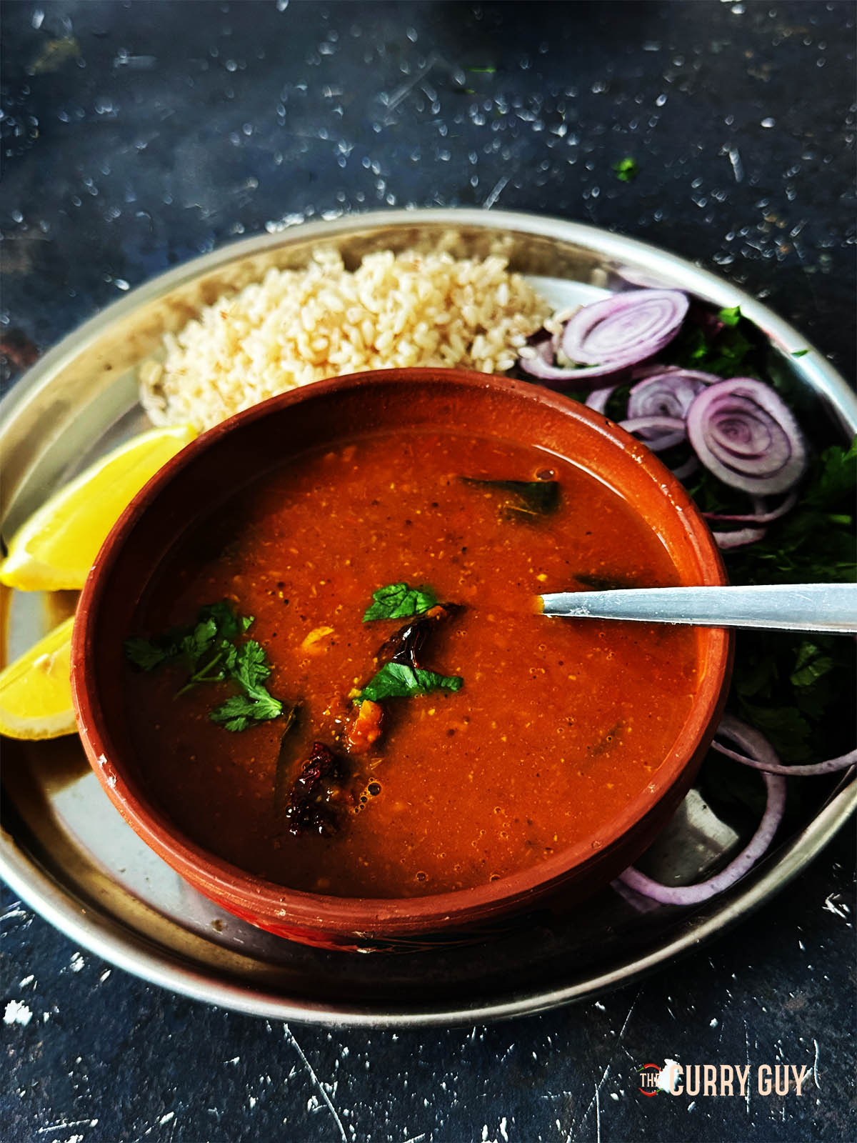 Hot rasam in a serving bowl with side salad and rice.
