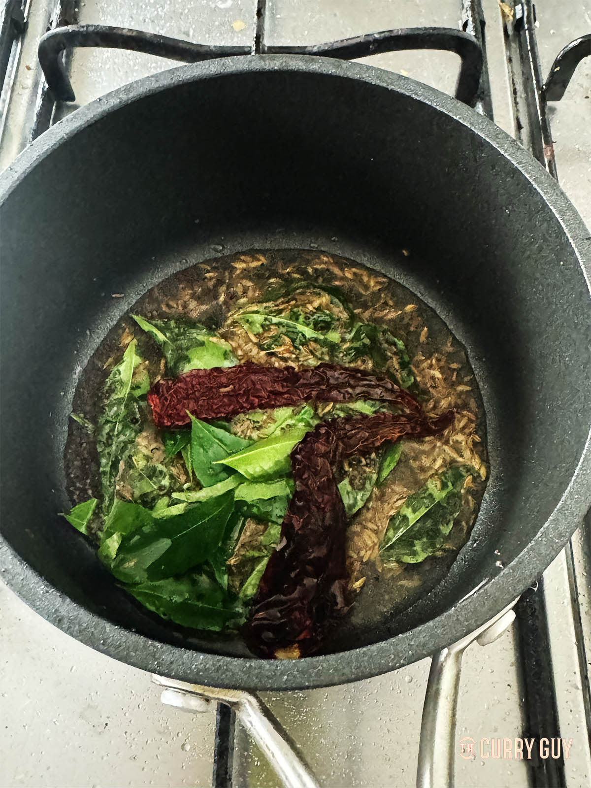 Adding mustard seeds, cumin seeds, curry leaves and dried chillies to coconut oil to make a tarka.