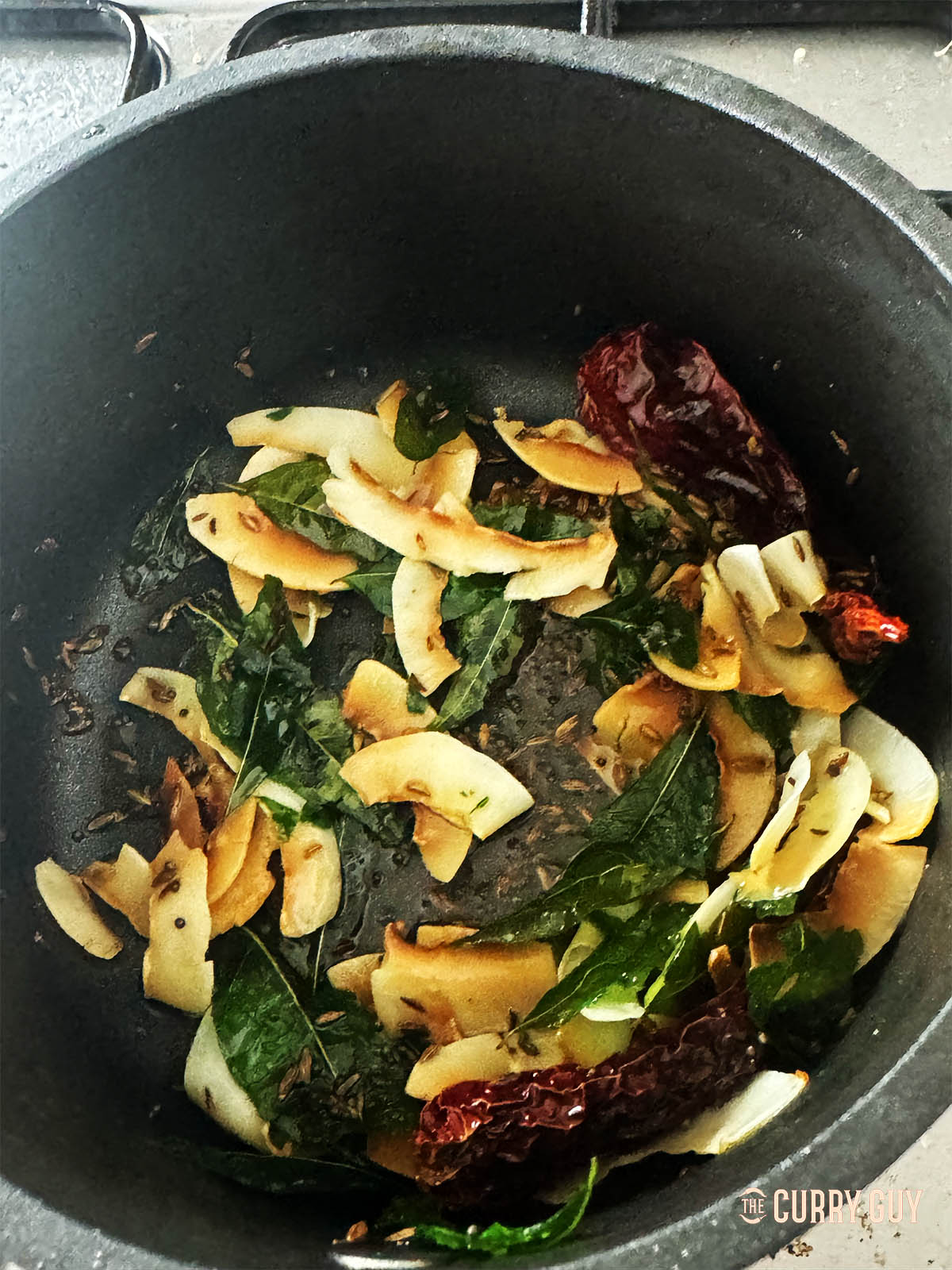 Adding flaked coconut to the tarka in the pan.