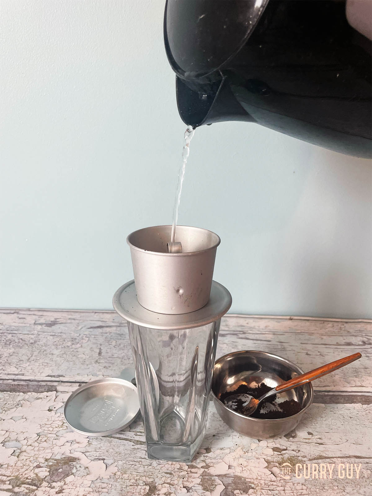Pouring water over the coffee grounds that are sitting in a filter above a glass. 