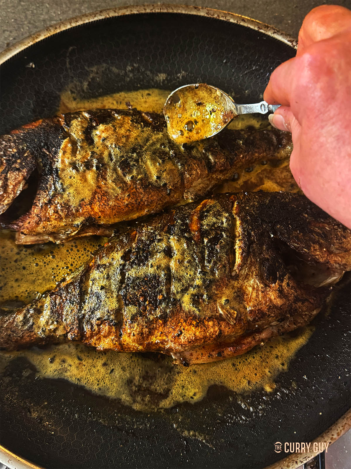 Basting the fish with the butter in the pan.