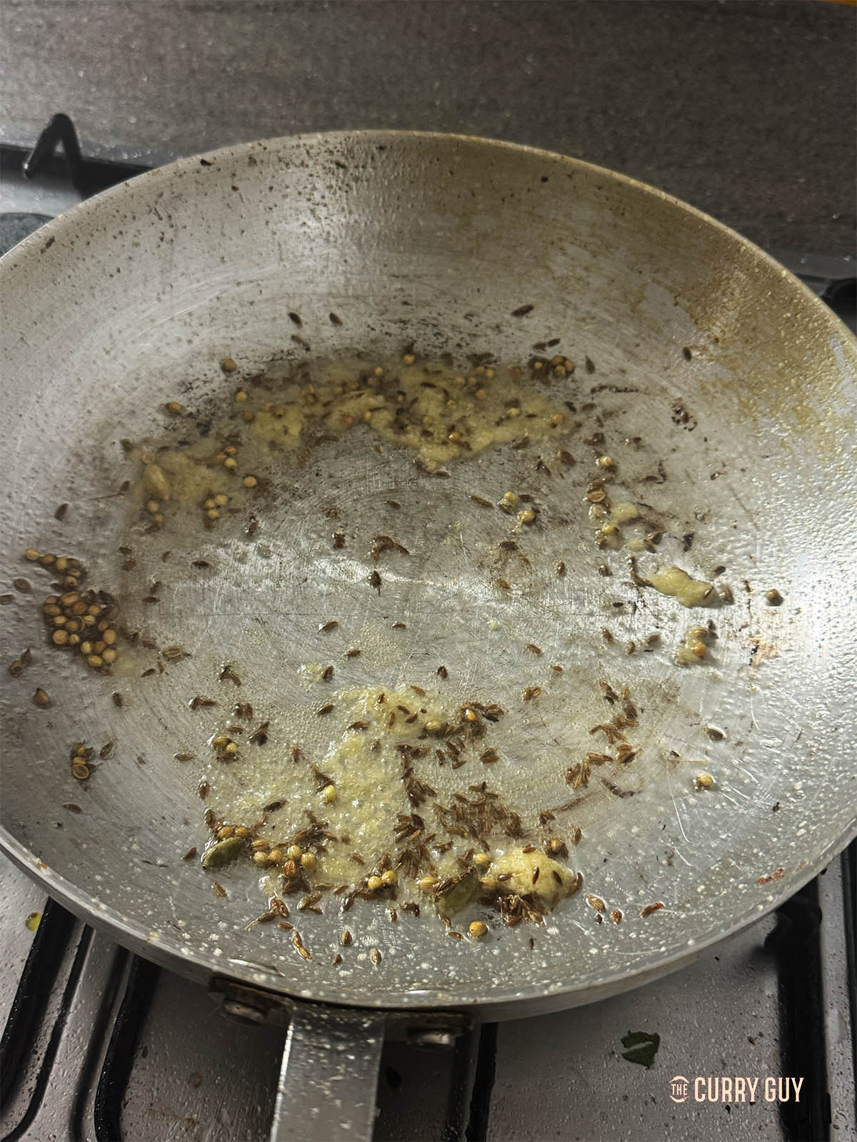 Adding the garlic and ginger paste to the whole spices in the pan. 