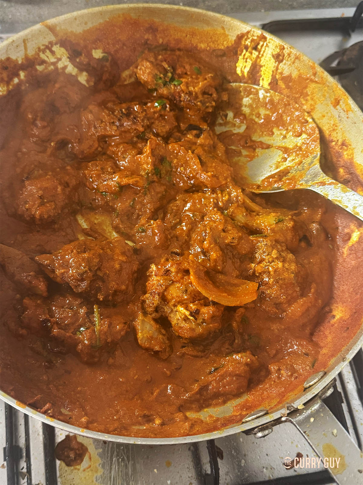 Stirring in the chicken and seasoning the sauce. Stirring in the onion and yoghurt paste.