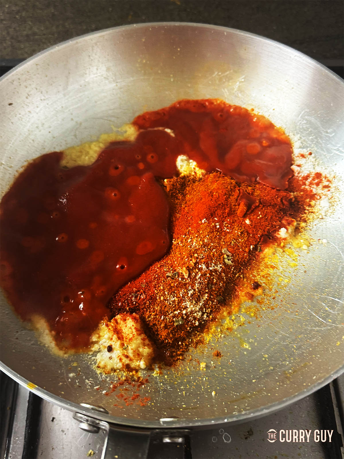 Adding the remaining spices to the pan with sugar, tomato puree and base sauce. 