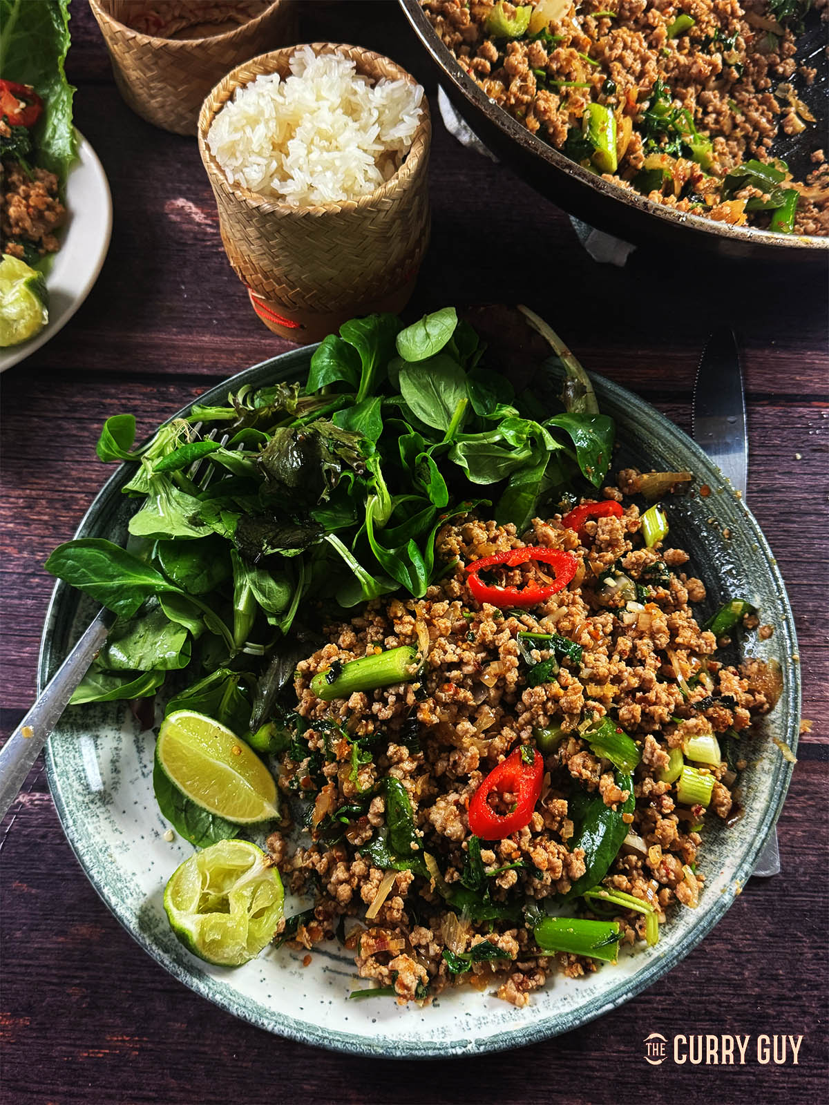 Pork larb on a plate next to sticky rice and salad.