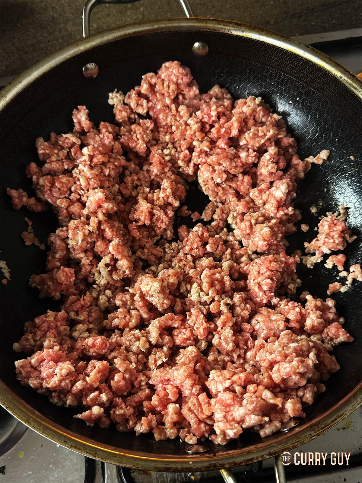 Adding the minced pork to hot oil to fry in a pan.
