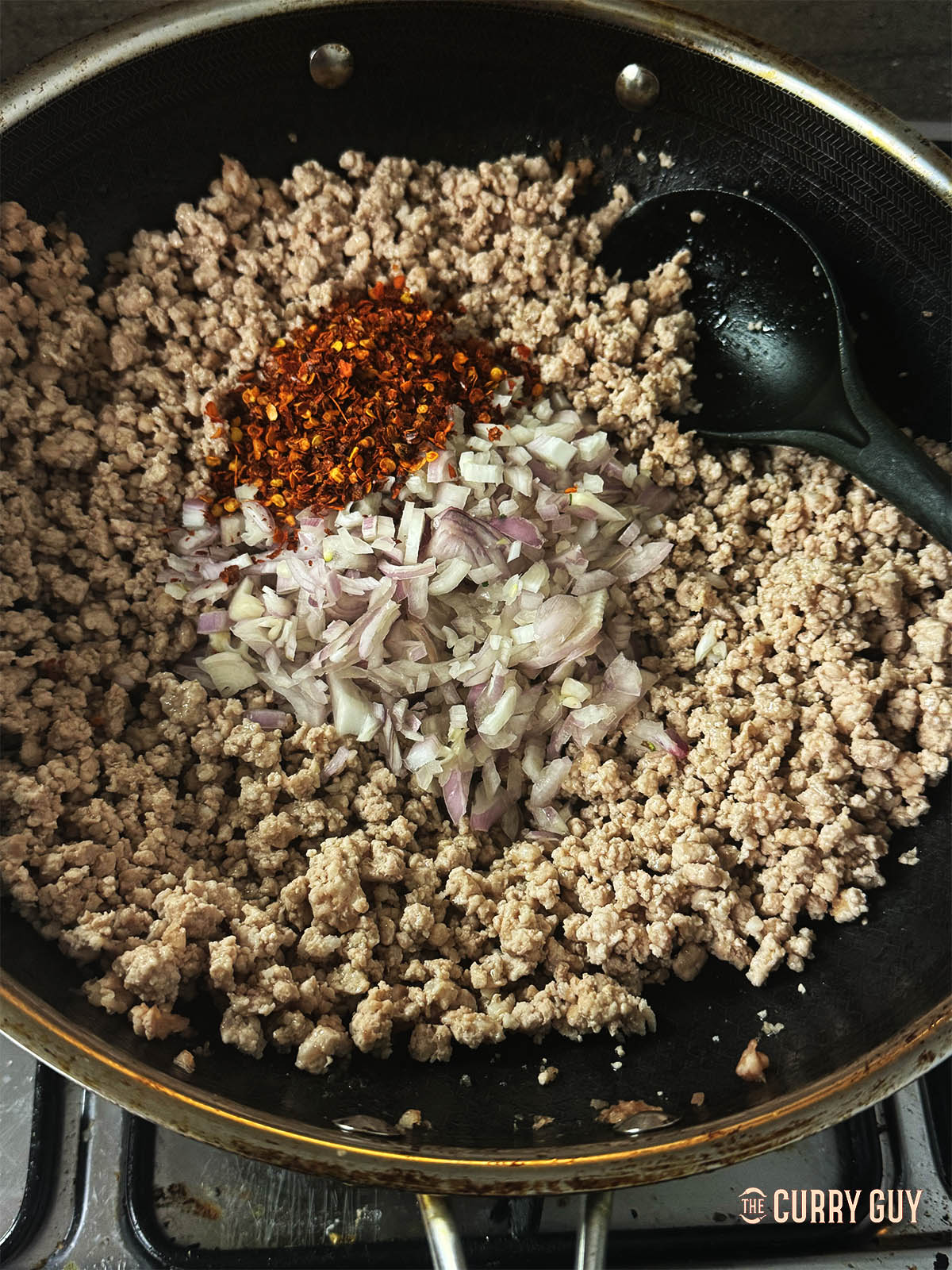 Adding chilli flakes and chopped shallots to the pork.