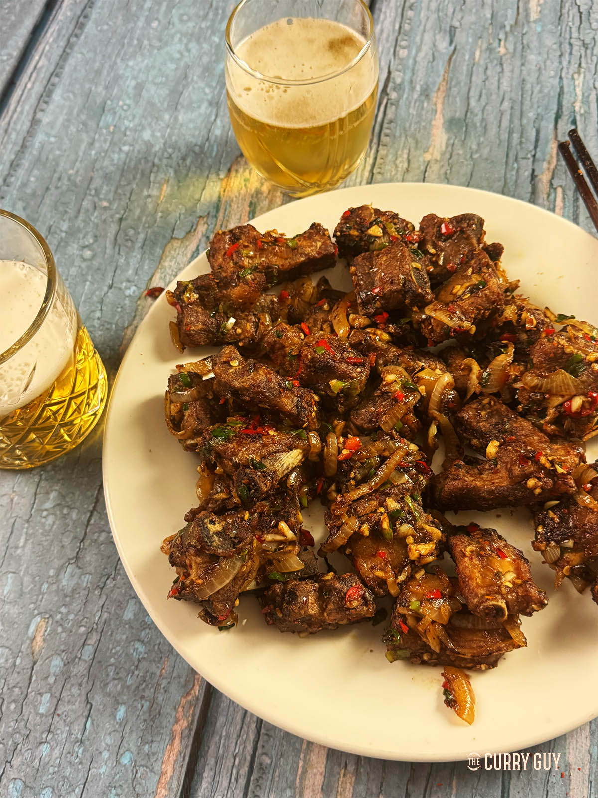 Salt and pepper ribs on a serving plate next to glasses of lager.